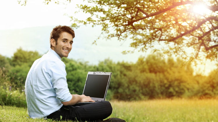 Smiling-at-camera-on-grass-and-laptop-1200x675